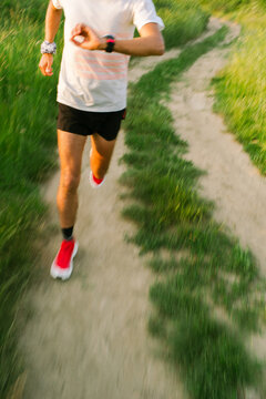 Runner Checks Watch While Jogging on a Path in Green Field