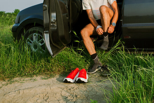 Man Puts on Red Shoes at Car During Sunny Day in Open Field