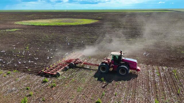 Tractor cultivating the soil in a field before planting, drone view.