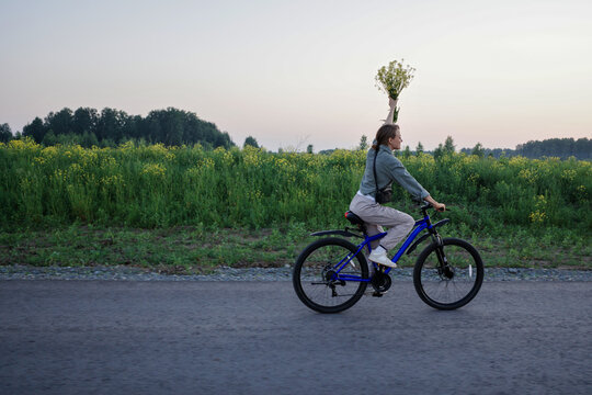 Woman riding bicycle with wildflowers in rural field at dusk