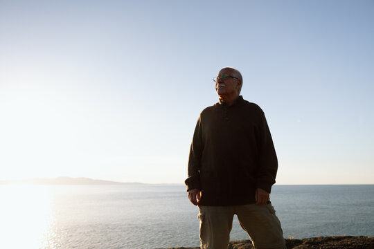 Senior man standing by the sea at sunrise, contemplative and calm