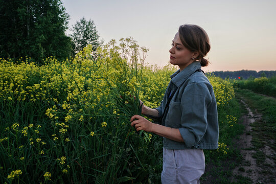 Woman holding yellow wildflowers in field at sunset