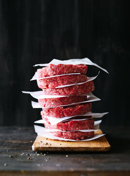 Beef patties stacked on a wooden board in a kitchen setting