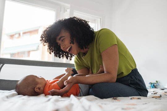 Mother laughing playing with baby on bed