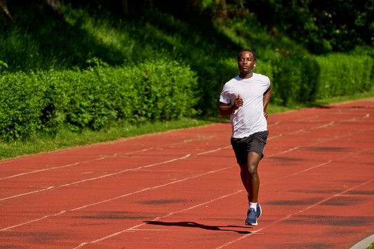 Man Runs on Track at Outdoor Sports Facility in Bright Sunshine