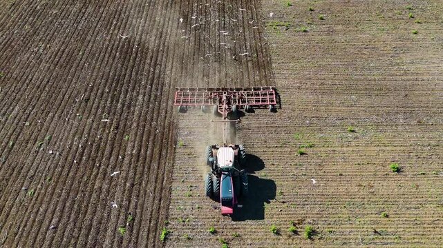 Tractor cultivating the soil in a field before planting, drone view.