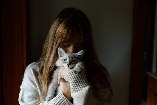Woman holding kitten close in cozy warm indoor portrait