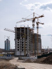 Construction site with tower cranes and high-rise building under development against a clear sky, urban architecture and building industry © Arrows