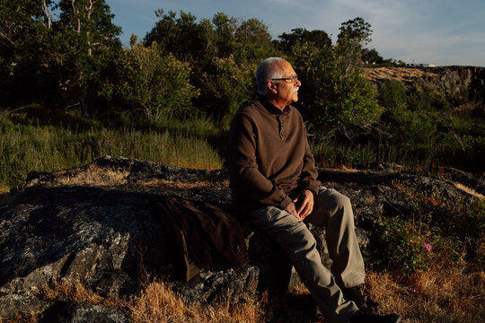 Elderly man sitting on rock, enjoying quiet nature moment