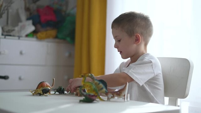 Child explores dinosaur toys at table. Child learns about dinosaur playing at home table. Child play with dinosaurs on table. Kid at table with dinosaur figures educational play. Child home dinosaur.