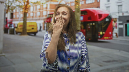 Fototapeta premium Senior hispanic woman with hand to mouth blowing a kiss on a city street by buses and shops; warmth kindness welcome connection.