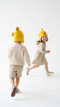 Two happy kids wearing yellow chicken hat running on white background