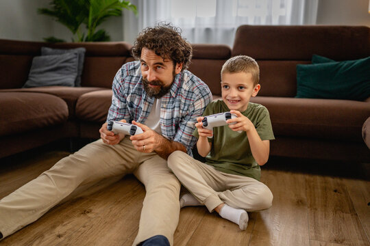 Father and son playing video games together on the living room floor, sharing a joyful moment