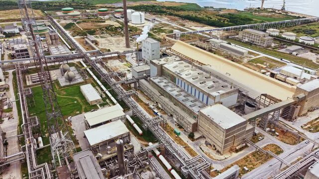 A large industrial area features various buildings and extensive pipelines. The site is close to the coast, showing the layout of the complex and its infrastructure.