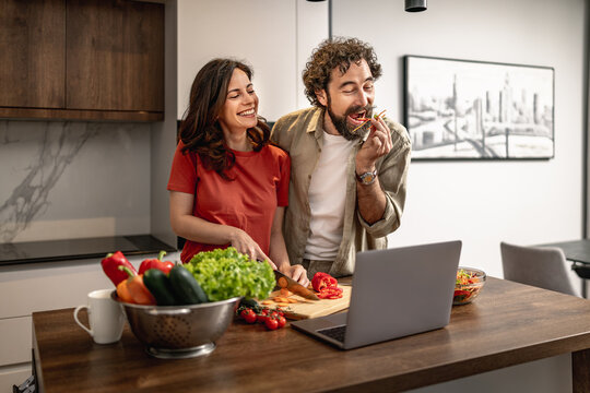 Happy couple cooking a healthy meal together in a modern kitchen while following an online recipe