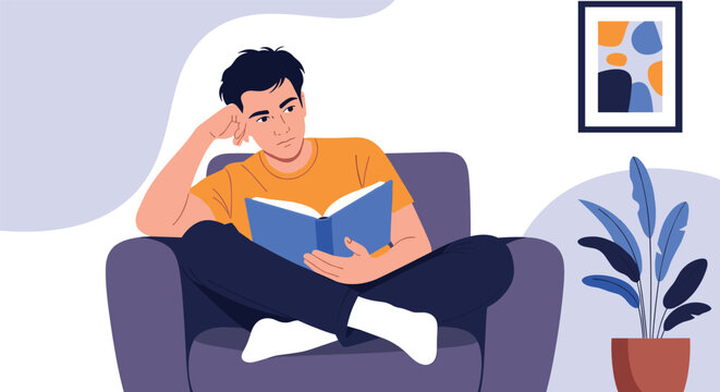 Young man sitting comfortably in a cozy armchair reading an interesting book in his modern living room.