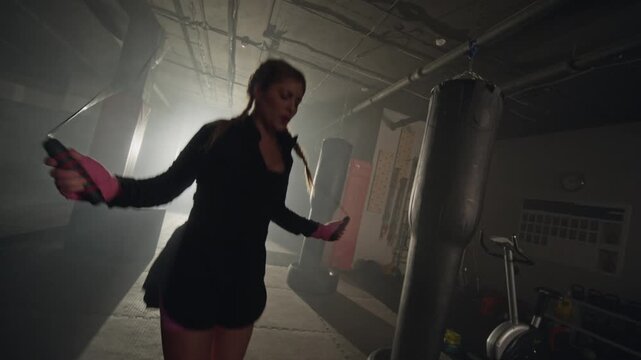 Young Caucasian woman skipping rope during intense cardio workout in boxing gym. Footage is perfect for fitness brand advertisements and gym promotions