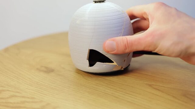 Man is breaking ceramic lamp base on a wooden table. Close up.