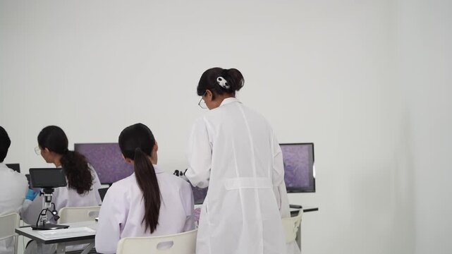 Instructor points to a feature of magnified purple tissue on a monitor as a seated laboratory team studies the screen during a group pathology teaching session