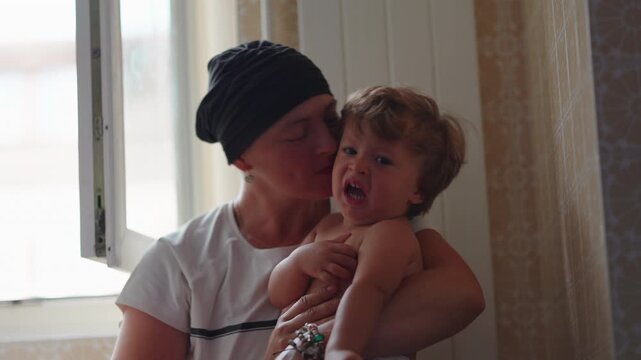Mother kissing toddler on the cheek during candid moment of affection, expressing comfort, attachment and unconditional parental love