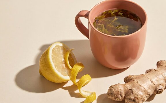 Pink mug of herbal tea with lemon peel and fresh ginger root