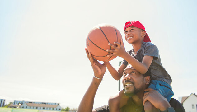 black father and young boy playing basketball on a court, teaching little player and spending time outdoors