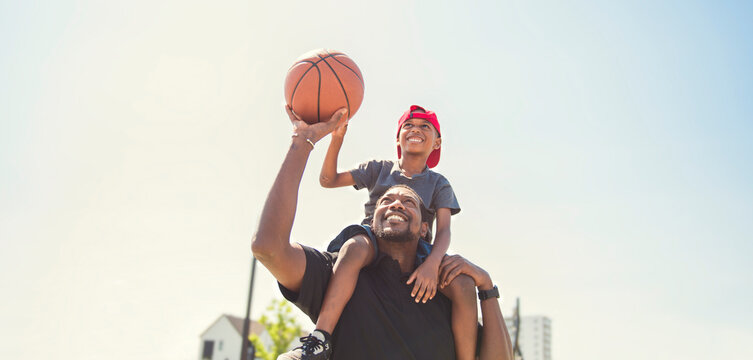 black father and young boy playing basketball on a court, teaching little player and spending time outdoors