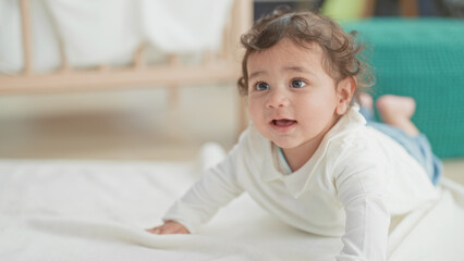 Fototapeta premium Girl on tummy shows face and hands pushing up, mouth open and gazing upward beside a crib in a nursery; curiosity.