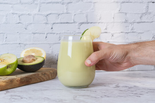 Hand holding green healthy smoothie made with avocado and apple