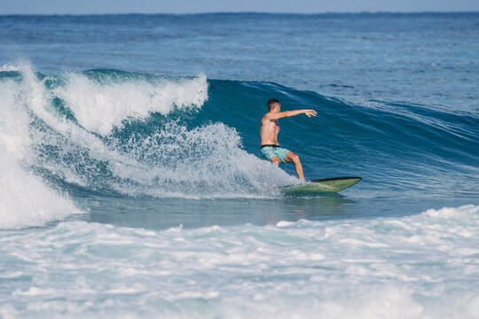 Athletic surfer riding a blue ocean wave on a sunny day