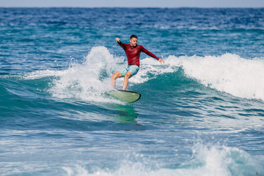 Surfer carving across turquoise ocean waves in sunlight