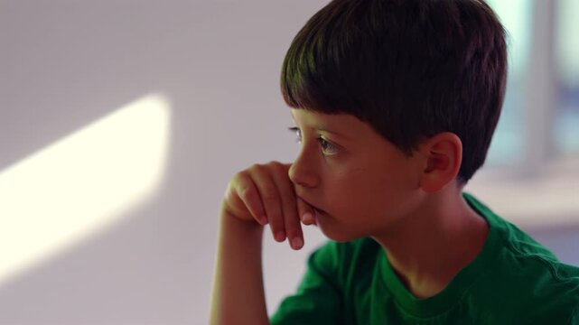Thoughtful child resting chin on hand, quietly observing surroundings with reflective expression