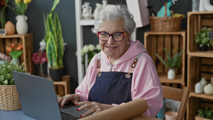 Fototapeta premium Woman florist typing on laptop with hands on keyboard in studio among shelves of flowers and plants; serenity craft.