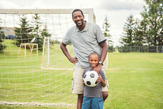 father with son playing football or soccer outside on field