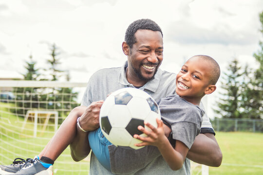 father with son playing football or soccer outside on field
