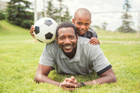 father with son playing football or soccer outside on field