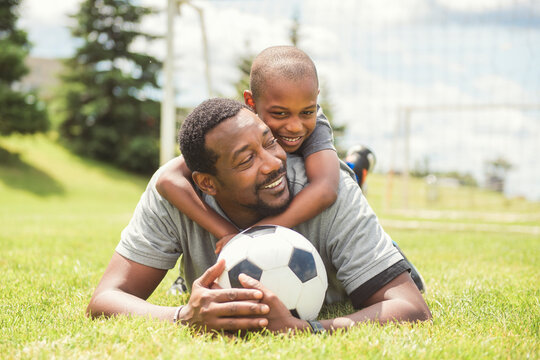 father with son playing football or soccer outside on field