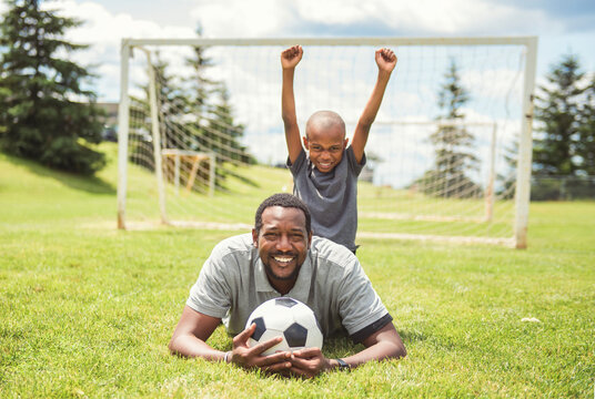 father with son playing football or soccer outside on field