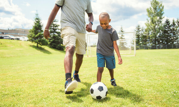 father with son playing football or soccer outside on field