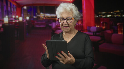 Senior woman holds tablet and taps screen with finger in rooftop lounge building  contentment digital connection. © Krakenimages.com
