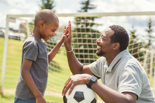 father with son playing football or soccer outside on field