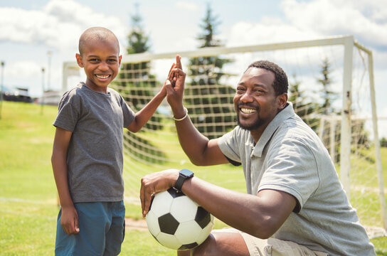 father with son playing football or soccer outside on field