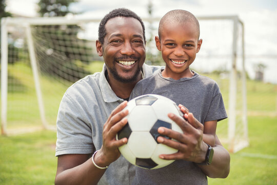 father with son playing football or soccer outside on field