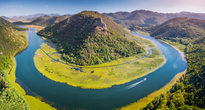 Aerial view of a boat navigating the scenic winding river, surrounded by lush green mountains and water lily meadows