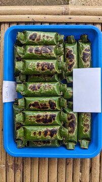 Authentic Asian street food delicacy grilled rice wrapped in banana leaves, perfectly charred and presented in a vibrant blue tray, natural lighting.