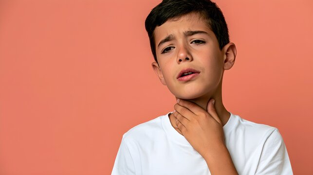 Young boy with hand on throat looking unwell with sore throat or illness against a plain background