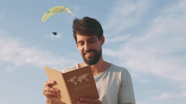 Adventurous man reading travel book with paraglider flying