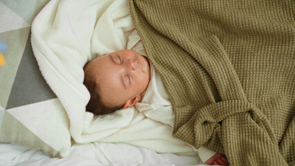 Baby sleeping on bed and cradle with bare hand peeking from under knit blanket on soft pillow in building  peaceful rest. © Krakenimages.com