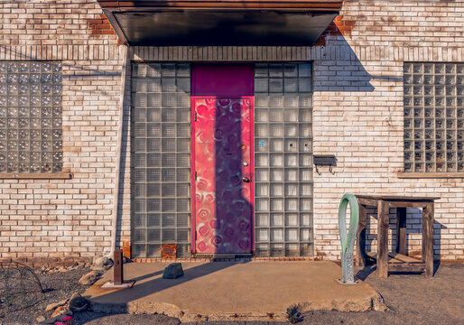 Derelict white brick building with glass block windows and sidelights, steel painted door at sunset, nobody