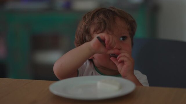 Toddler eating yogurt with spoon at dining table, encouraging self feeding, healthy nutrition and fine motor development